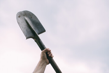 A man's hand holds a bayonet shovel on a white background. Metal shovel in his hands against the sky