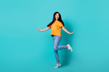 Fototapeta na wymiar Full size photo of cool brunette lady dance wear orange t-shirt jeans sneakers isolated on turquoise color background