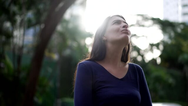 Thoughtful woman standing outside looking at sky in contemplation. Pensive person lost in thought