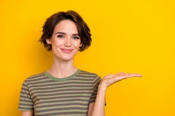 Closeup photo of young funny smiling cute woman holds hand promotion empty space new product isolated on yellow color background