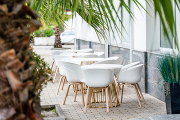 Street cafe with white chairs, green foliage around. Without people, tourism, travel.