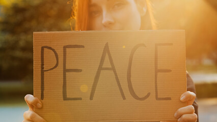 Close up female hands hold cardboard with written word peace symbolic banner attractive young woman...