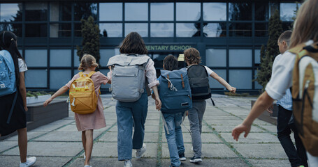Diverse children going school with backpacks. Teachers welcoming teen students - obrazy, fototapety, plakaty