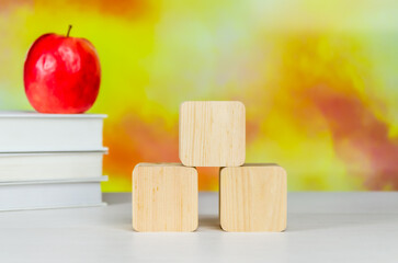 Stack of books, Red apple, colored pencils and cubes on desktop on blurred autumn background
