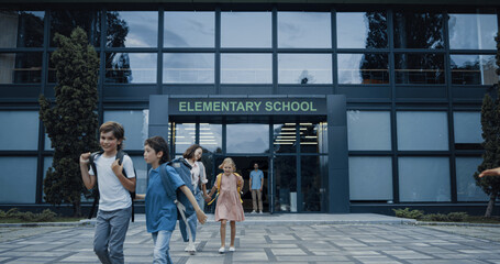 Pupils leaving elementary school building. Children smiling walking outside. 