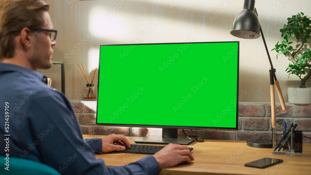 Poster Young Handsome Man Working from Home on Desktop Computer with Green Screen Mock Up Display. Creative Male Checking Social Media, Browsing Internet. Living Room in Bright Loft Apartment.