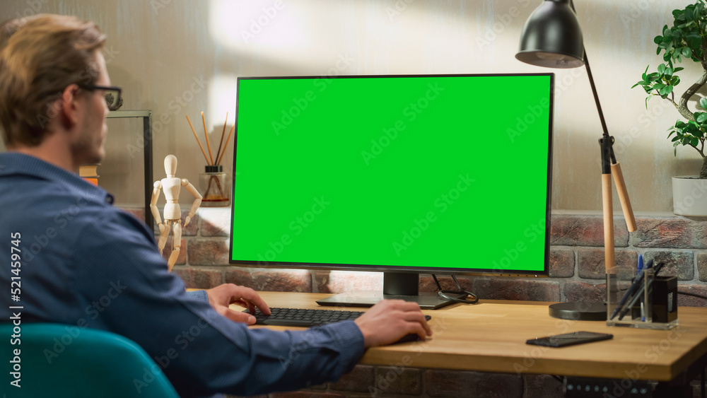 Poster Young Handsome Man Working from Home on Desktop Computer with Green Screen Mock Up Display. Creative Male Checking Social Media, Browsing Internet. Living Room in Bright Loft Apartment.