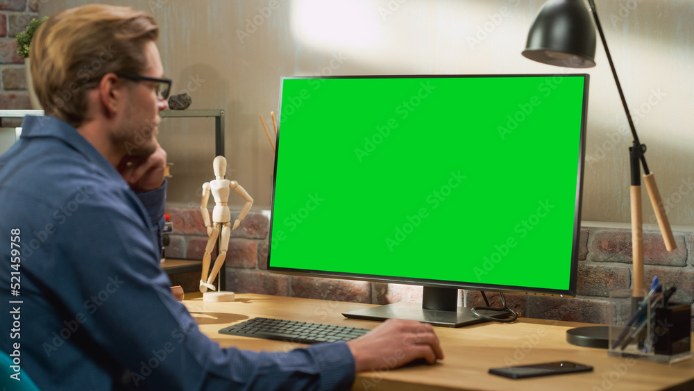 Poster Young Handsome Man Working from Home on Desktop Computer with Green Screen Mock Up Display. Creative Male Checking Social Media, Browsing Internet. Living Room in Bright Loft Apartment.
