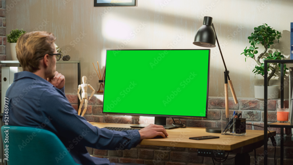 Poster Young Handsome Man Working from Home on Desktop Computer with Green Screen Mock Up Display. Creative Male Checking Social Media, Browsing Internet. Living Room in Bright Loft Apartment.