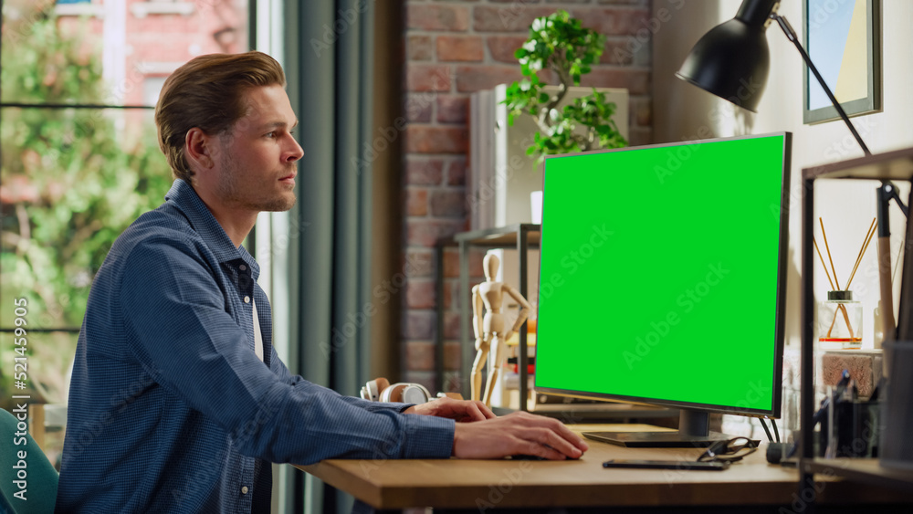 Poster young handsome man working from home on desktop computer with green screen mock up display. male che