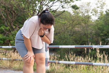 Medium shot, young obese Asian woman standing at outdoor park, resting after running, unable to breathe, suffering from respiratory problem. Health issues, heart attack, heat stroke, obesity concept. - obrazy, fototapety, plakaty