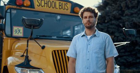 Thoughtful bus driver standing in front yellow vehicle looking camera close up.