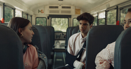 Three teenagers sitting school bus talking alone. Smiling girl taking seat.