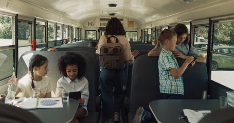 Teenage pupils boarding school bus. Diverse children using gadgets in vehicle.