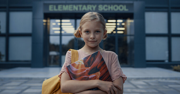 Little School Girl Posing At Campus Door Close Up. Blonde Child Holding Books