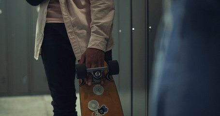 Boy hand holding skateboard with stickers in school hall close up. Hobby concept