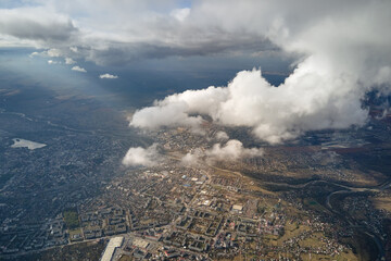 Aerial view from airplane window at high altitude of distant city covered with white puffy cumulus...