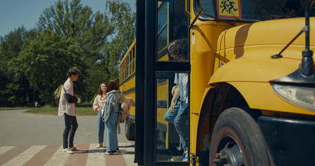 Two pupils leaving schoolbus chatting. Teenagers standing talking near bus.