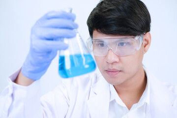 Asian male scientist hold test tubes with blue liquid chemical in laboratory.