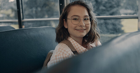 Smiling school girl sitting at bus window in glasses. Student looking camera.