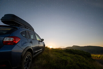 Fototapeta na wymiar Blue offroad SUV car with roof trunk on background of very beautiful night starry sky after sunset. Freedom and travel by car concept