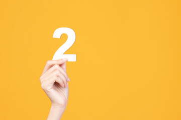 Hand holding wood number on yellow background.