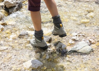 woman with mountain boots while looking at the stream walking over the stones