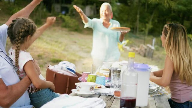 Smiling grandmother  bringing sweet food to family at picnic table in backyard