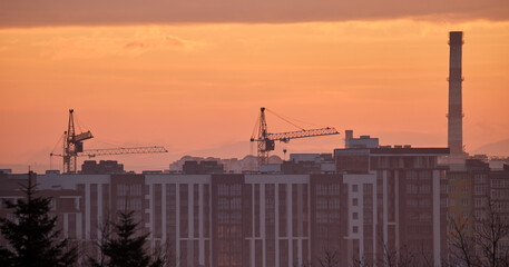 Dark silhouette of tower cranes at high residential apartment buildings construction site at sunset. Real estate development