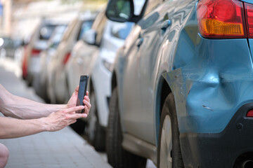 Stressed driver taking picture on sellphone camera of smashed vehicle calling for emergency service...