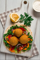 Tortillas, wrapped falafel balls, with fresh vegetables, vegetarian healthy food, on a wooden white background, no people, selective focus.