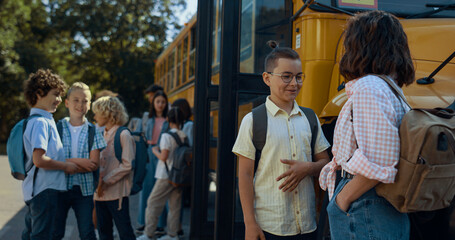 Students waiting schoolbus boarding. Pupils standing talking at yellow shuttle.