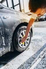 A man washes his car with foam at a self-service car wash, wheels and tires close-up