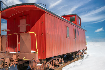 Vintage red wooden train caboose on rails in a snowy field, daytime, sunny, nobody
