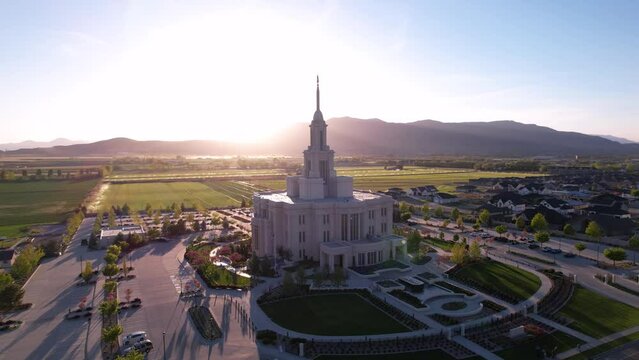Aerial 360 degree footage of Payson Utah Temple in the middle of trees and houses under the blue sky