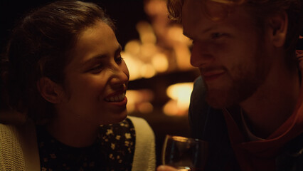 Closeup girlfriend boyfriend talk by home fireplace. Couple drink clink glasses.