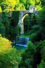 Enchanting view of Cecco Bridge in Ascoli Piceno with the pure waters of the Castellano river gently flowing below and some thriving green vegetation flourishing all around on a great summer day