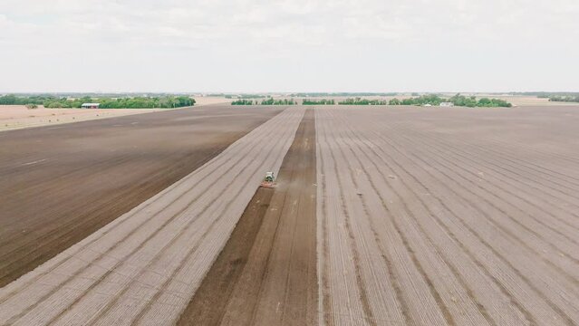 Aerial static footage over the tractor working in the brown agricultural fields