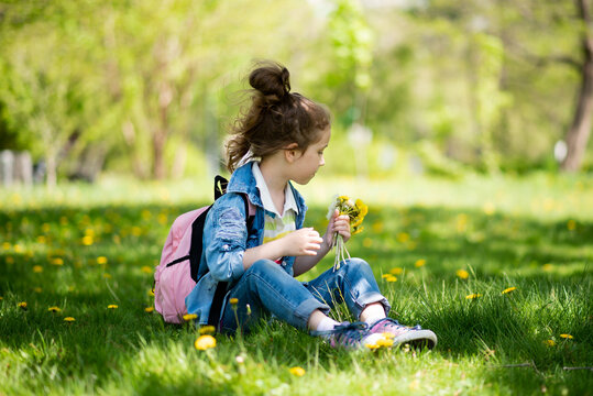 A sweet girl of five years on a walk. It's spring outside and the sun is bright. A girl holds a dandelion in her hands. She is wearing a colored T-shirt and a denim shirt. Childhood. Family.