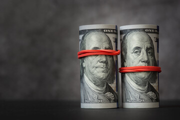 Rolls of hundred-dollar bills with red rubber bands on them, covering mouth and eyes of Franklin's...