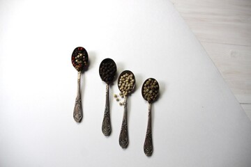 Silver spoons with spices of green, white, black peppercorn and pepper mix on white background