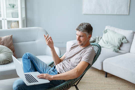 mature man using a laptop while sitting in a home chair.