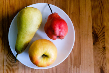 Two pears and an apple lie on a white plate. View from above. Copy space