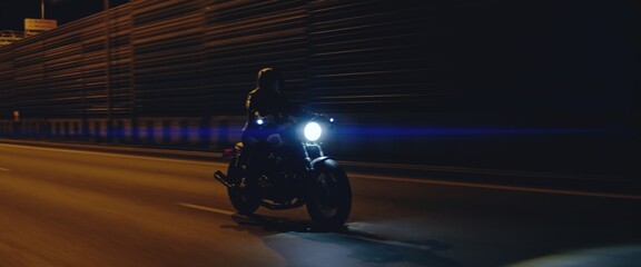 Biker riding his custom built cafe racer motorcycle through city at night. Shot with 2x anamorphic lens