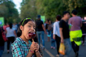 Fototapeta premium A happy girl eating caramel apple at a fair.