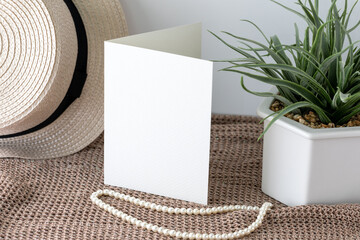 Blank white invitation card in vertical lay on knitted cloth with beach hat and pearl lace.