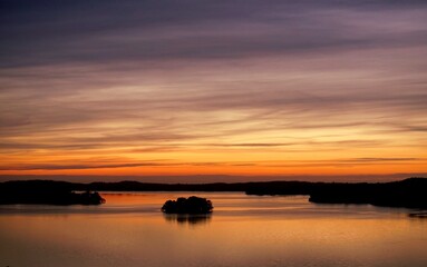 Fototapeta na wymiar Sonnenaufgang am See Himmel gefärbt ähnlich Regenbogen von bläulich-lila bis orange-rot Silhouetten von Bauminseln auf dem See