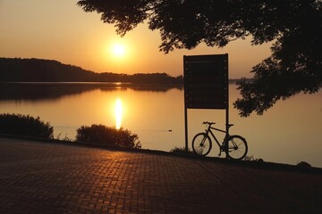 Blick auf einen See bei Sonnenuntergang Silhouette von Bäumen Schild Fahrrad Spielgelung...