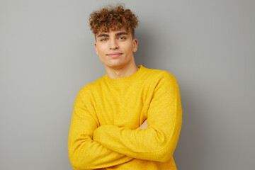 a self-confident pleasant man stands on a gray isolated background in a bright sweater and looks...