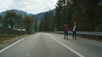 Happy tourists hitchhiking car on highway. Smiling friends wave hands on nature.